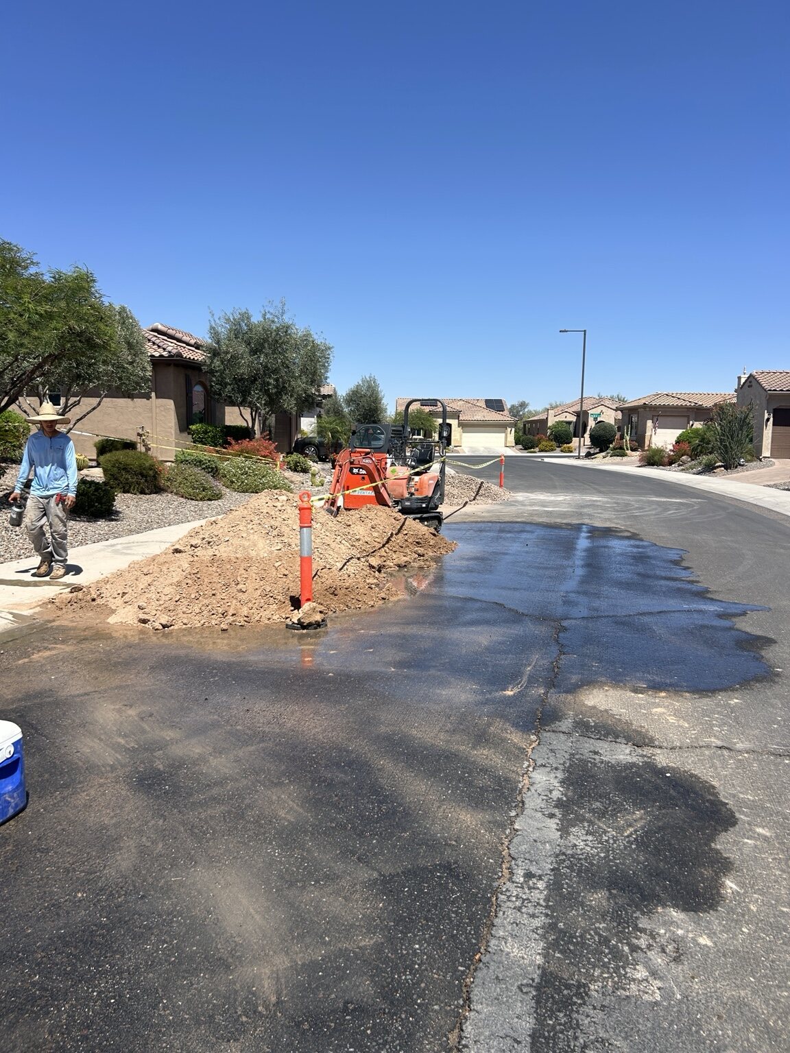 Excavation area beside a residential street with a small orange excavator