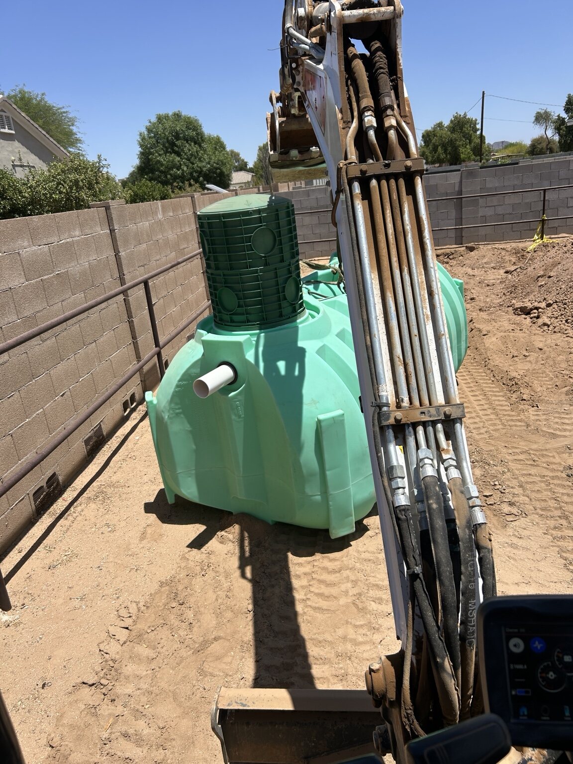 Excavator beside a large green underground tank on a job site