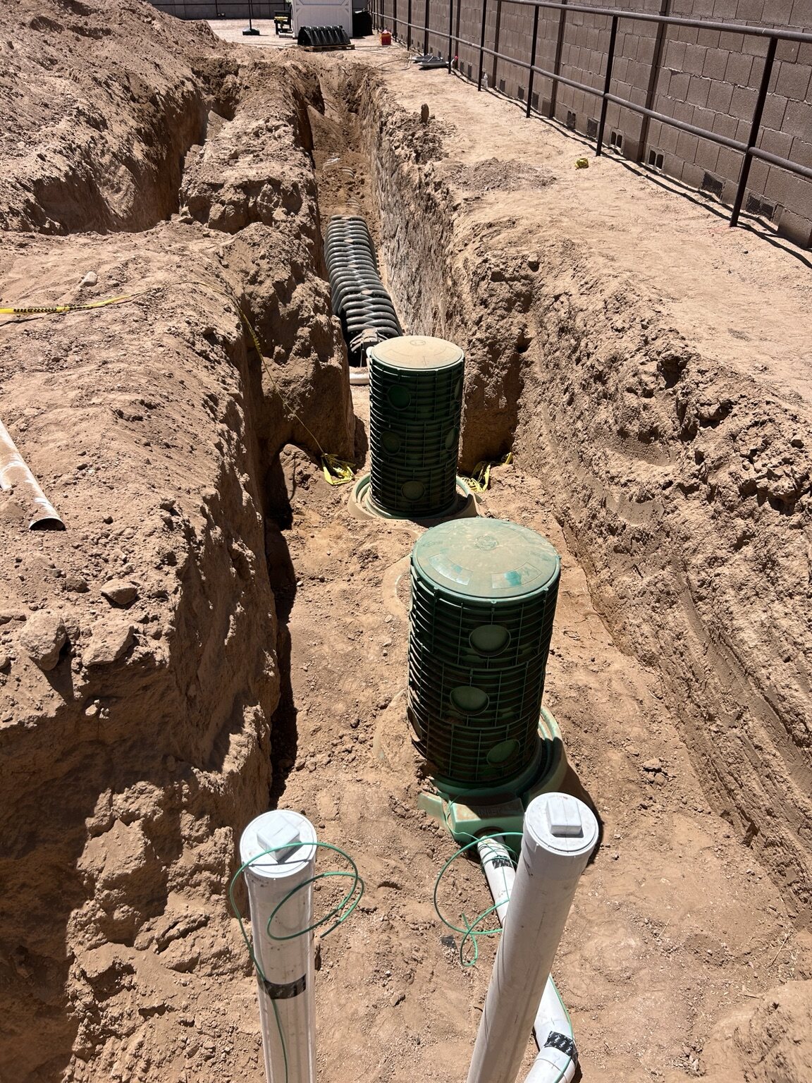 Green underground access risers and piping in an excavated trench
