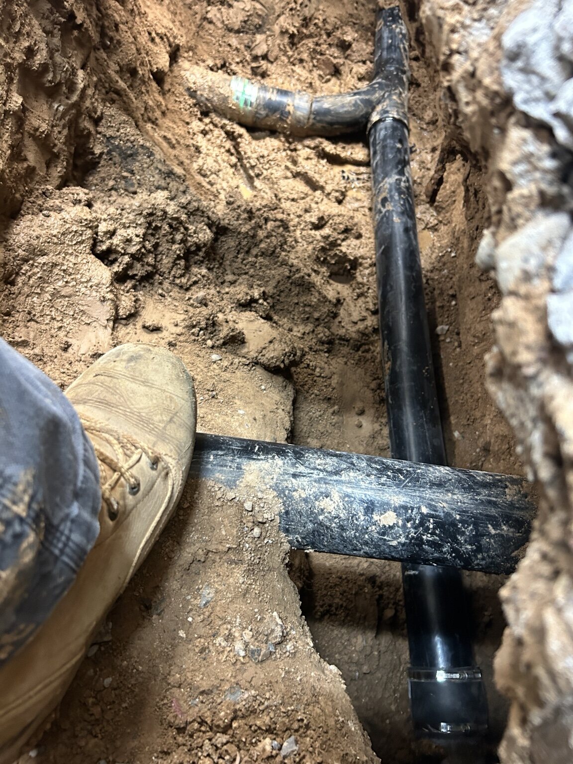 Black piping and fittings exposed in a narrow trench