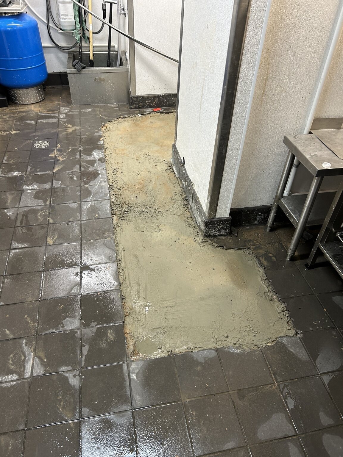 Fresh concrete filling a section of floor beside existing tile