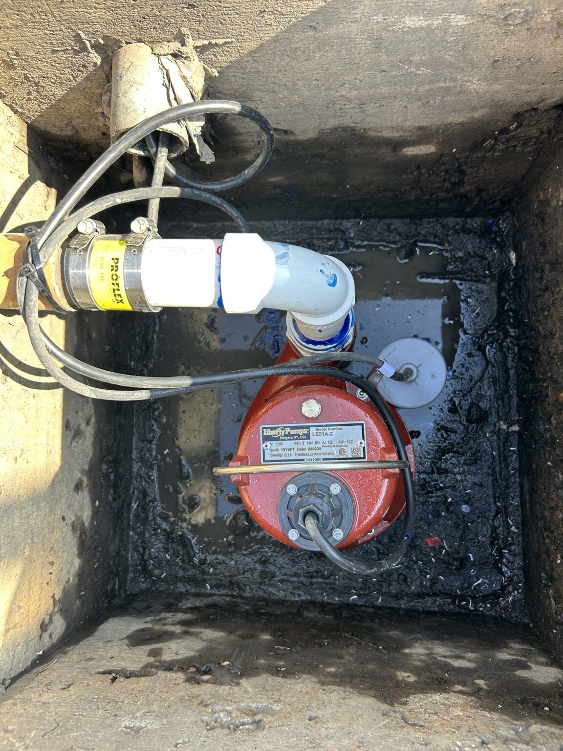 Red pump connected to white piping in a below-grade access pit