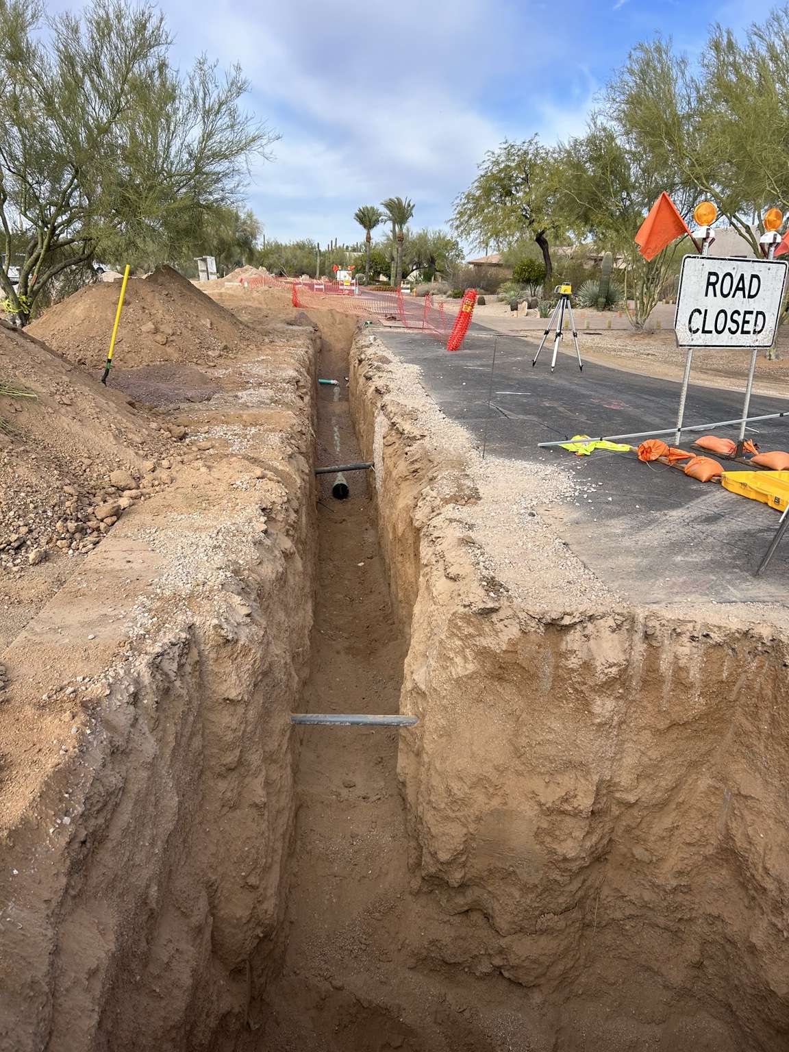 Deep utility trench with safety barriers and a road closed sign along an Arizona residential street