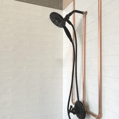 Black shower fixtures and exposed copper piping against white tile